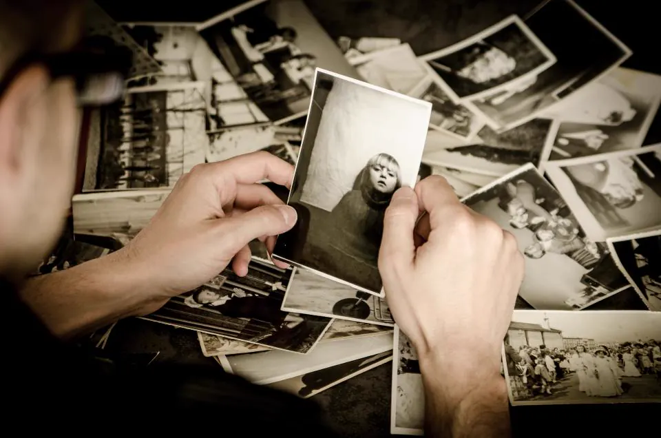 Unas manos sostienen una fotografía antigua sobre una pila de recuerdos familiares en blanco y negro